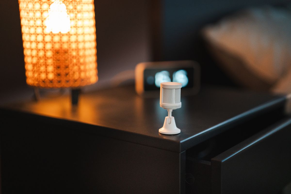 A bedside table with a motion sensor, lamp and clock