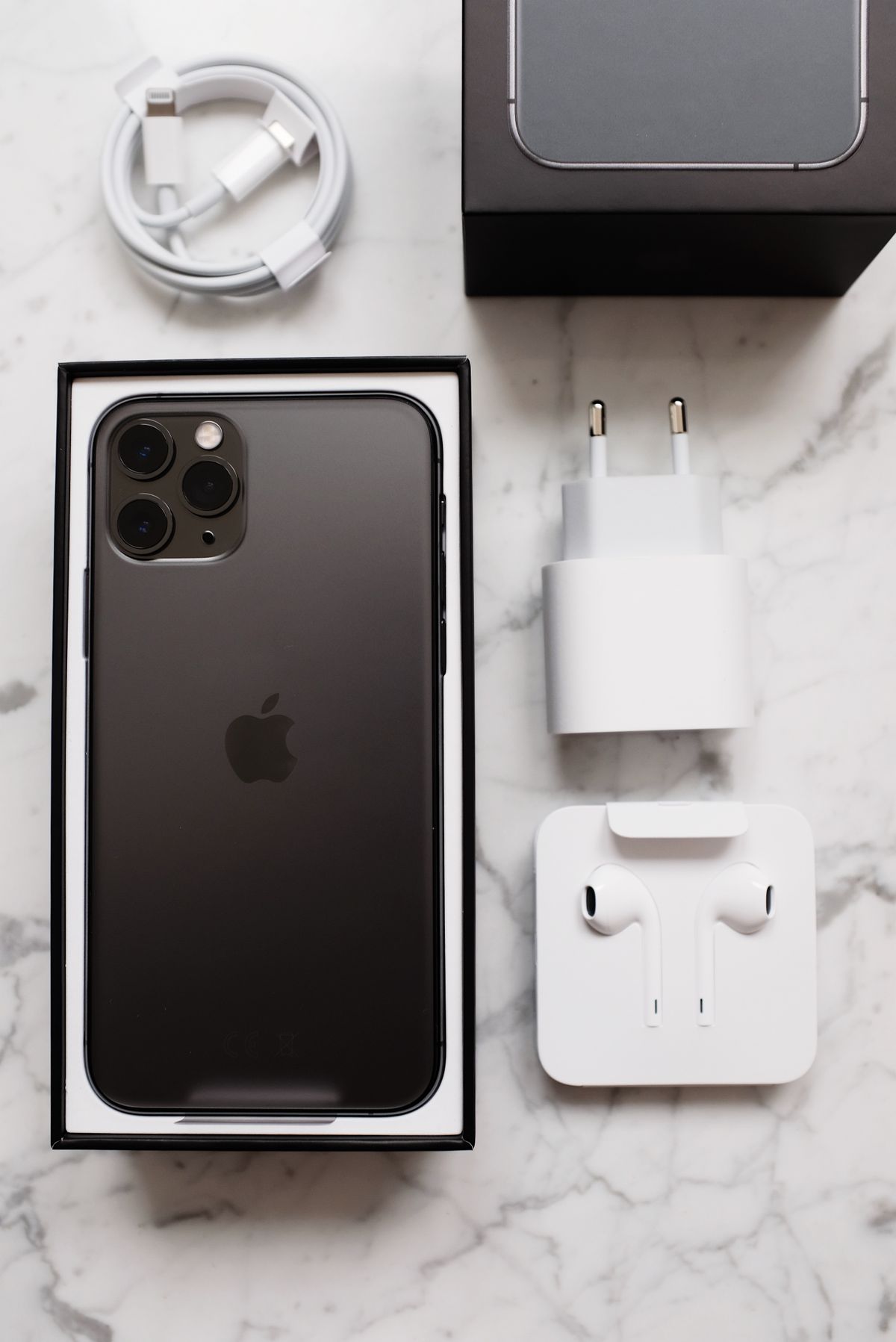 A phone, charging cable and earphones arranged on a marble desk