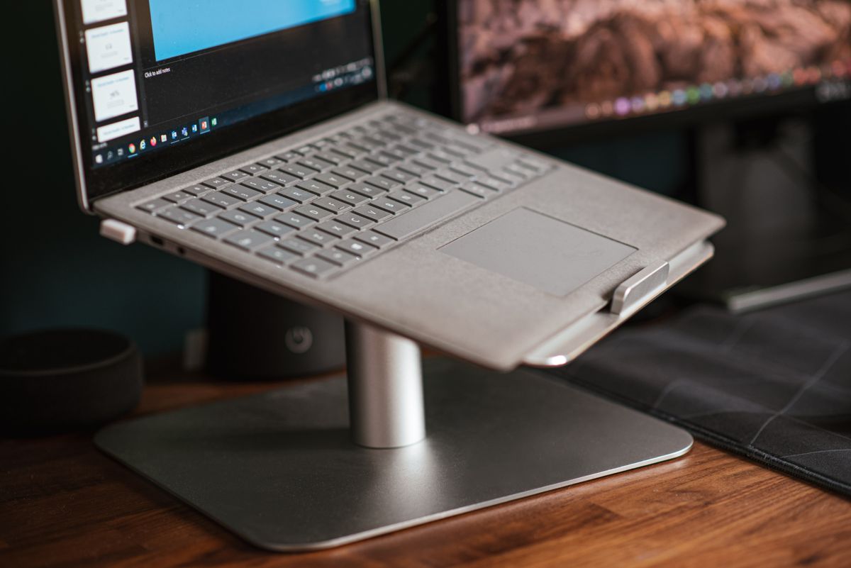 A laptop raised on a stand beside a monitor on a work desk