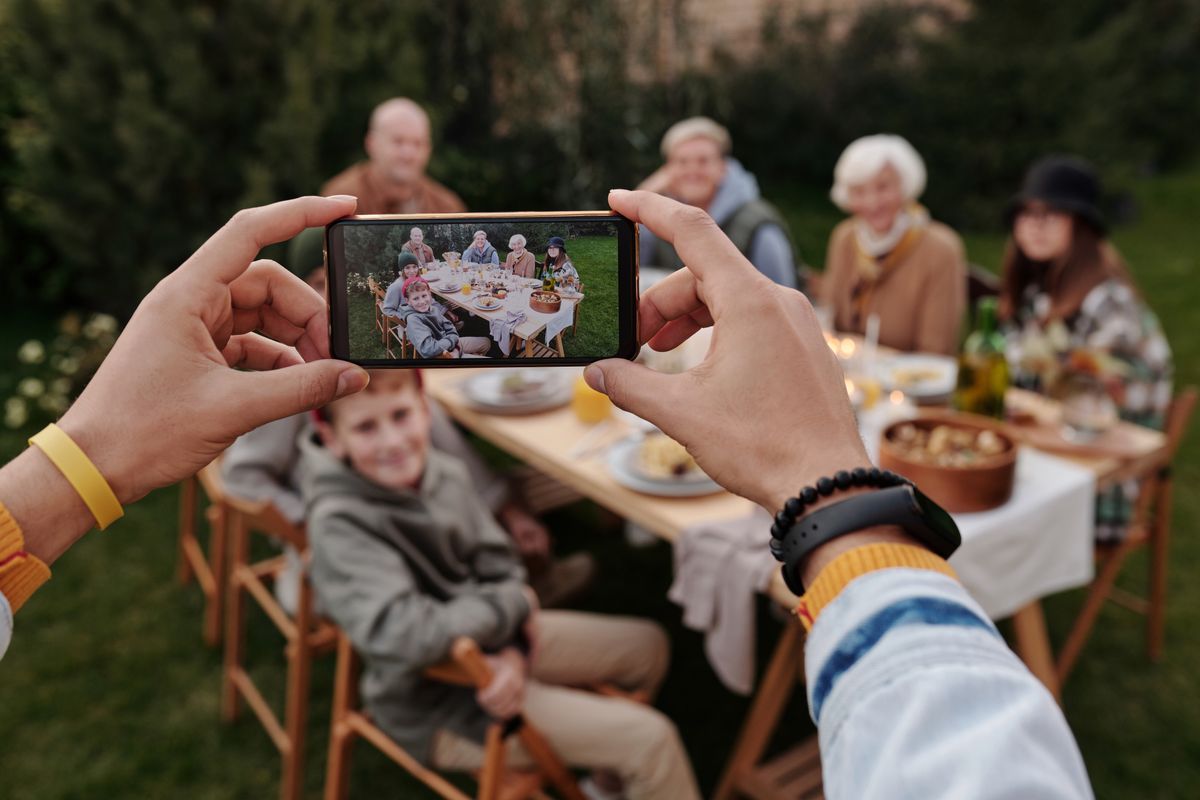 A hand holding a smartphone to photograph an outdoor family meal