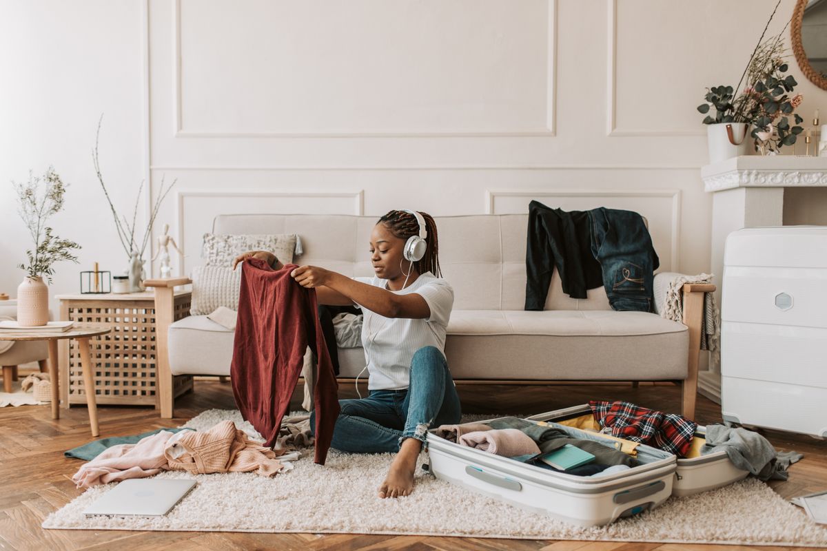 A woman wearing headphones while packing a suitcase at home